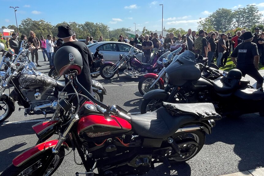 Motorbikes parked with a crowd of people standing behind them.