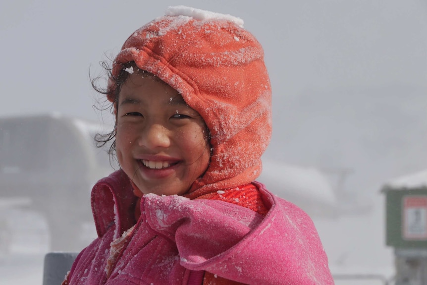 A child smiles while wearing a snow-covered hooded jacket.