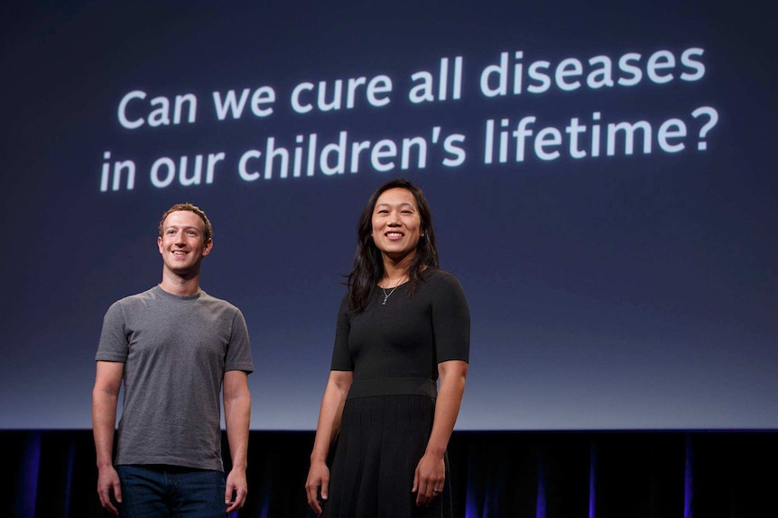 Mark Zuckerberg and Priscilla Chan stand in front of a screen saying "Can we cure all diseases in our children's lifetime?"