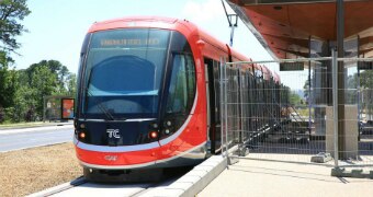 Red and black tram at a station with construction fencing around the stop.