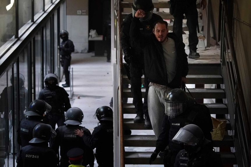 A man holding up a fist up is led down a staircase by numerous black-clad police.