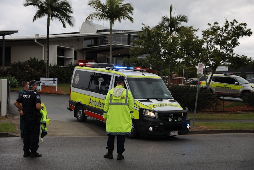 Police in yellow high-vis directing an ambulance out of a police station driveway