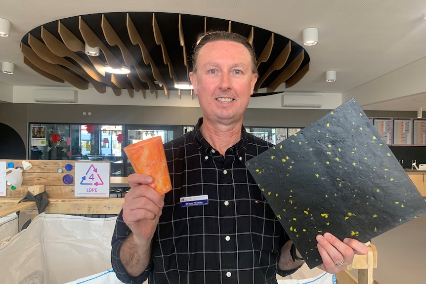 A male teacher holds plastic prototypes, one orange cup and one black sheet.