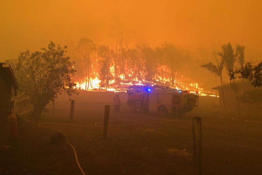 A fire truck surrounded by flames in bushland.