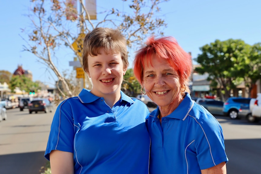 young business owner standing next to her mother. Both women are smiling and wearing a blue uniform