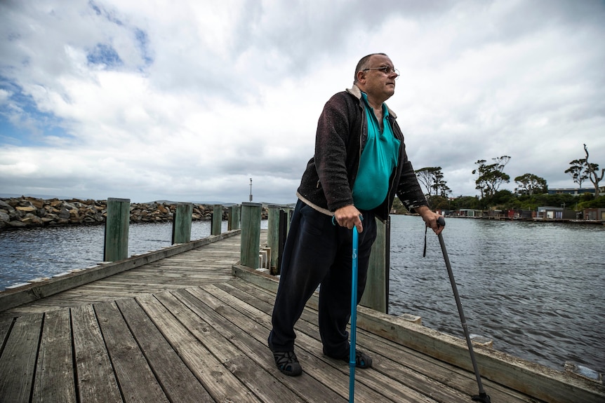 Craig Ayers using walking sticks on a jetty.