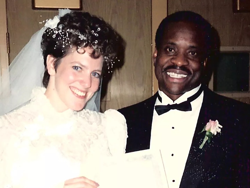 A couple in 80s wedding outfits smile at the camera
