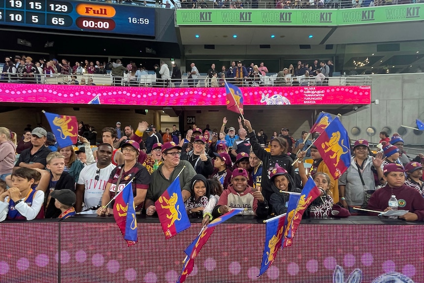 A group of Indigenous people waving Brisbane Lions flags at the Gabba