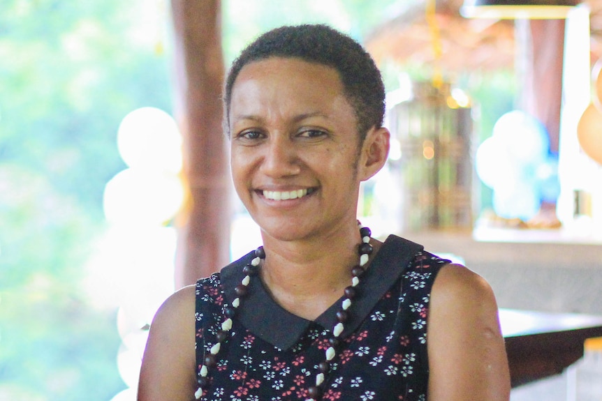 a woman wearing a beaded necklace smiles at the camera. 