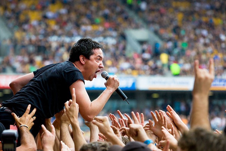 A man in a black shirt holding a microphone and singing to a large crowd of people.