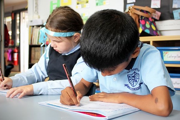 Image of two kindergarten students at their desks practising handwriting skills.