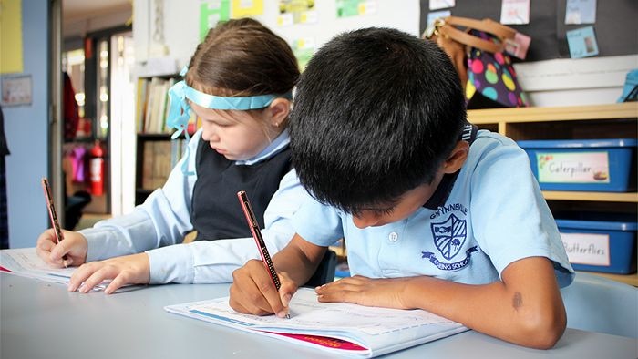 Image of two kindergarten students at their desks practising handwriting skills.