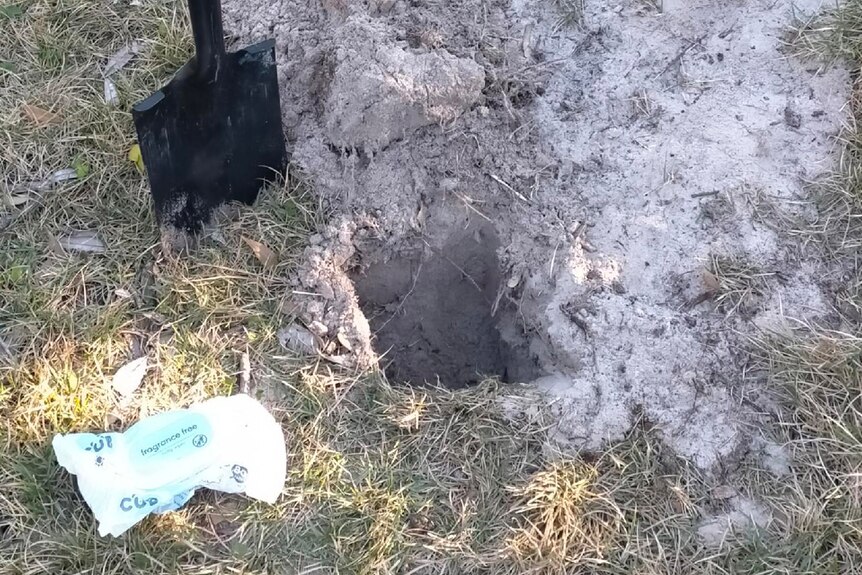 A shovel next to a hole in the ground makeshift toilet