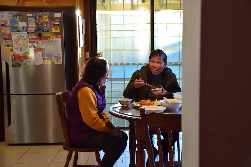 An older Asian couple sitting at a round dining table sharing a meal.