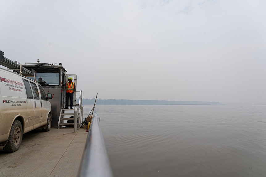 A car ferry floats across a grey, smoky river.
