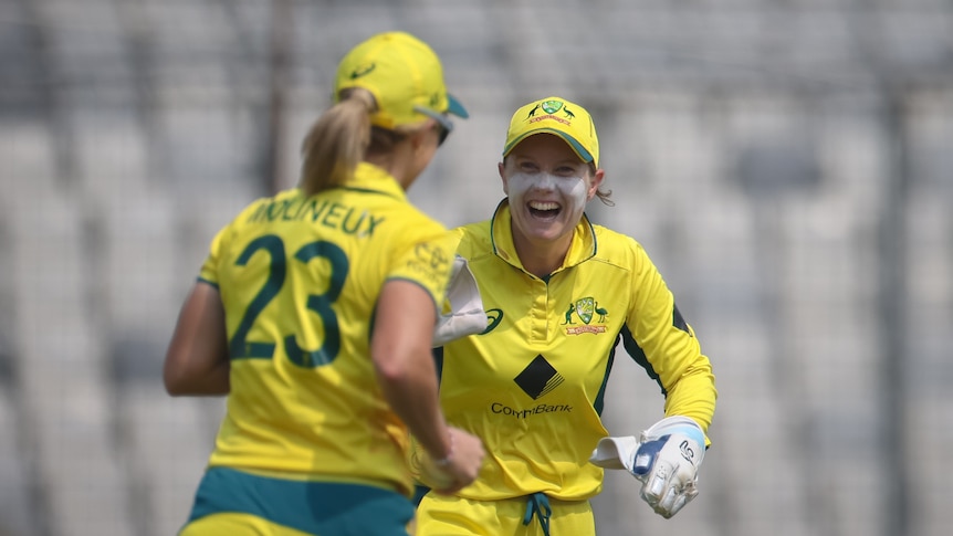 Australian women's cricket captain Alyssa Healy grins widely at her teammate after the team takes a wicket in a T20I.