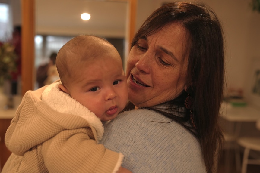 A middle aged white woman with brown hair holding a baby 