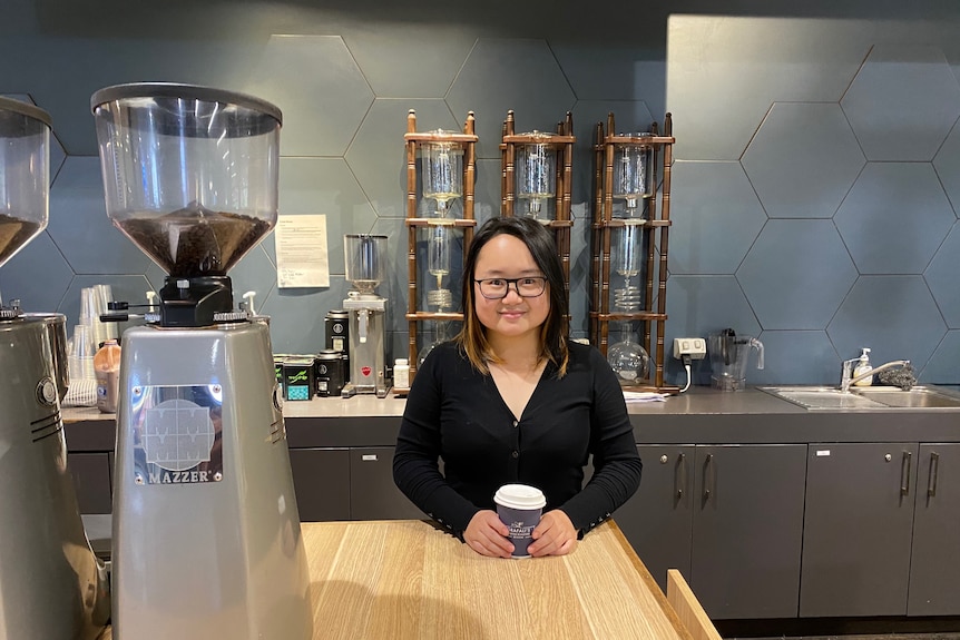 A woman stands in front of the counter at a cafe. 