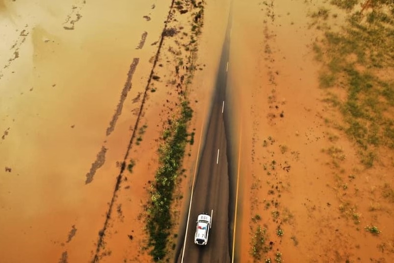 an aerial shot of a police car on a small section of highway, while the rest of the road and landscape are flooded.