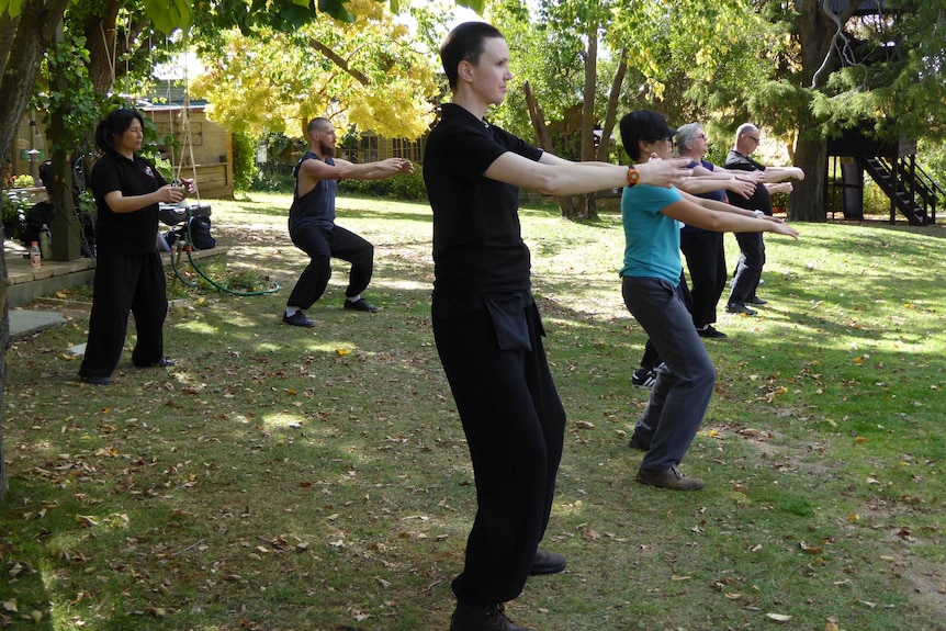 Six people hold their arms in front of them in a park.