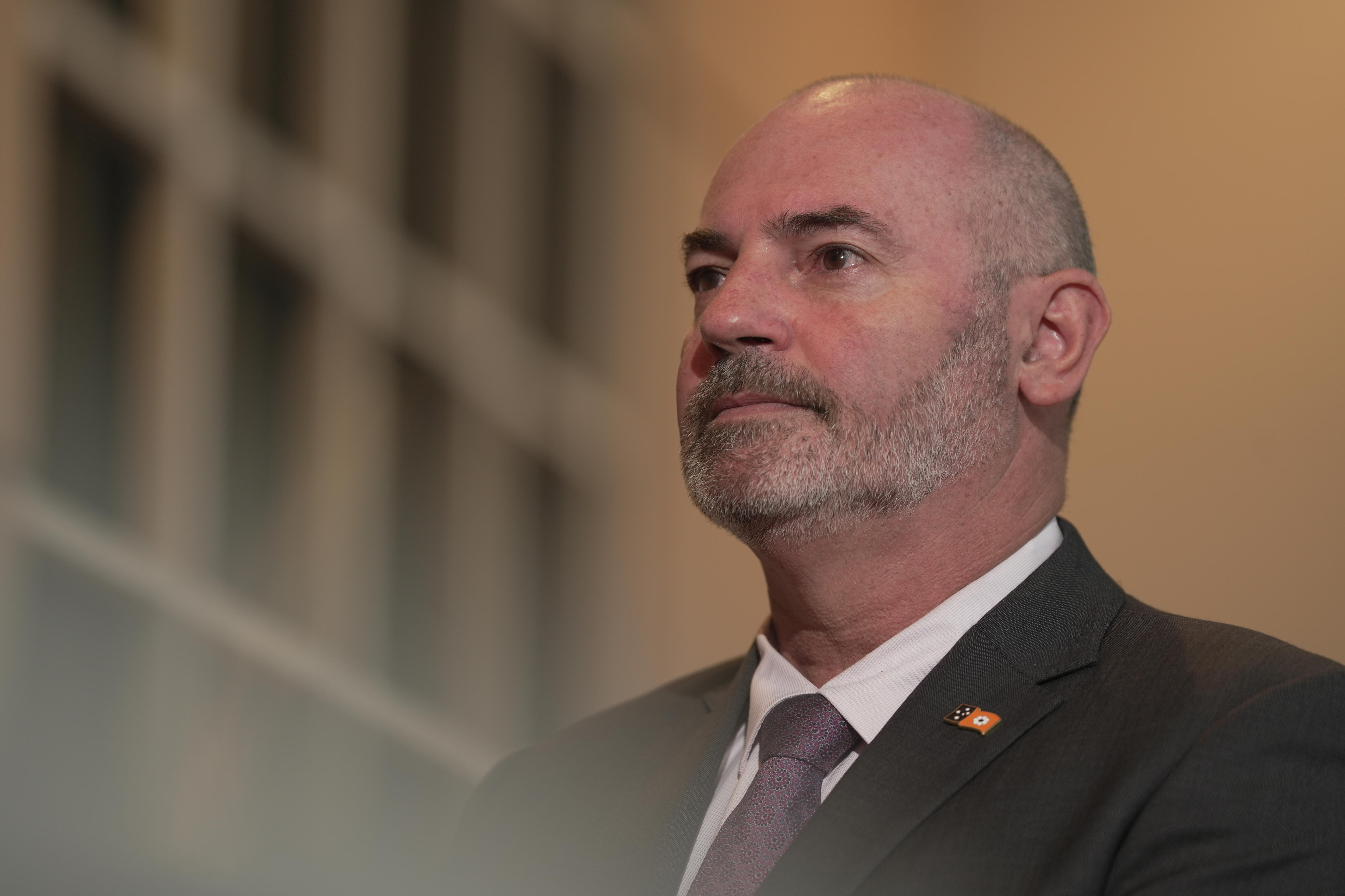     Un hombre con traje oscuro y corbata parece serio detrás de la cámara.