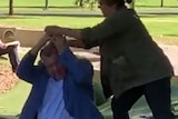 A screenshot of a video showing a woman with her hands above Craig Kelly's head.