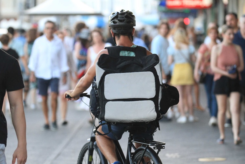 A food delivery rider on a bicycle with a crowd of people in the distance.