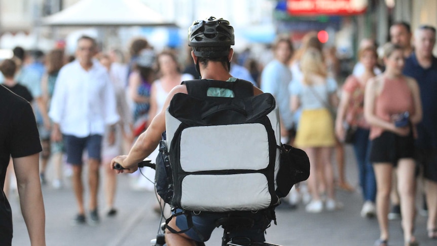 A food delivery rider on a bicycle with a crowd of people in the distance.