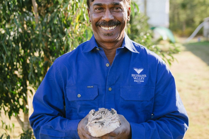 A man in a blue shirt holds a quail.