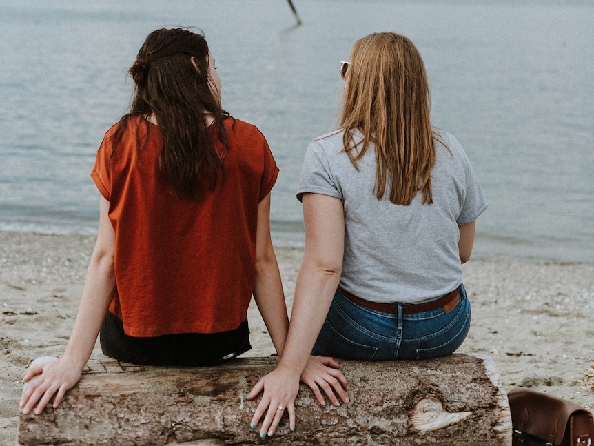 Two women sitting on a log at the waterside to show the need for space from your partner from time to time