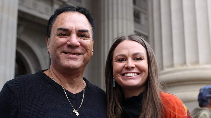 Sissy Austin and her father Neville Austin stand side-by-side smiling on the steps of Victoria's Parliament House.
