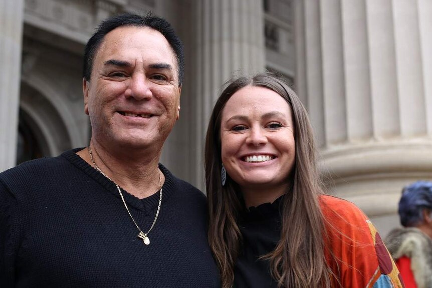 Sissy Austin and her father Neville Austin stand side-by-side smiling on the steps of Victoria's Parliament House.