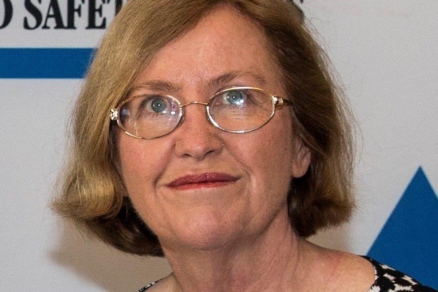 A woman with bobbed light brown hair and silver-rimmed glasses is smiling at the camera