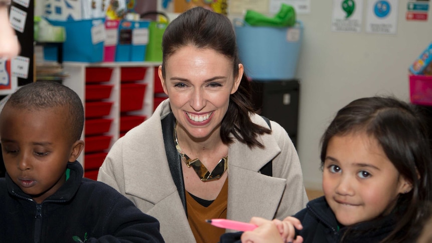 Jacinda Ardern smiles next to children in a school.