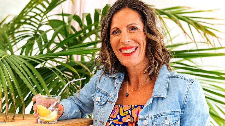 A woman stands next to a bench holding a drink.