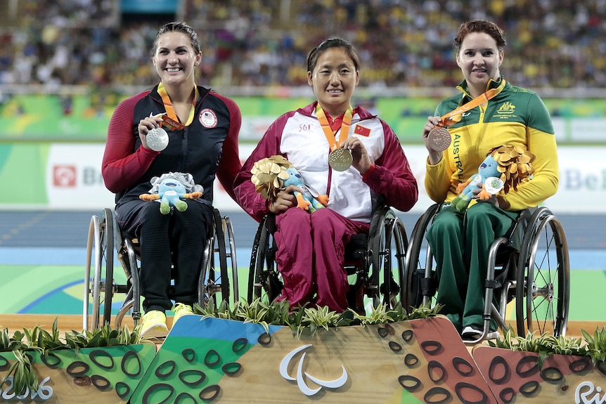Three Paralympic athletes sit in their wheelchairs holding their medals, with an Australian woman on the right..