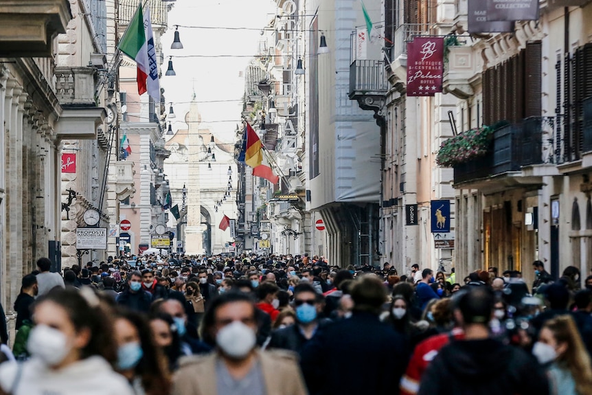 Una folla di persone in una strada di Roma durante il giorno indossando maschere per il viso