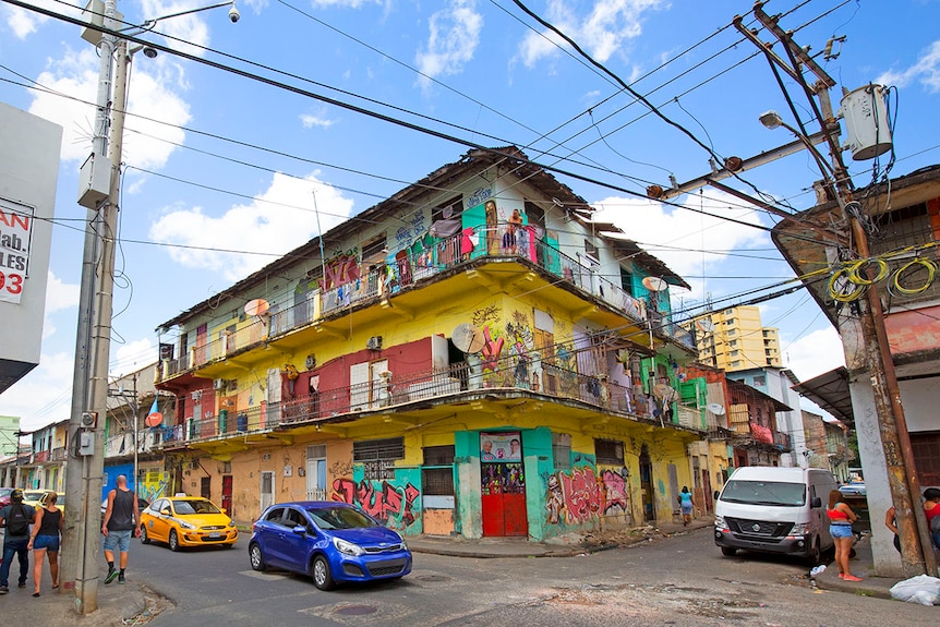 Locals stand out on the balcony of a bright yellow apartment block, watching victor show tourists down the street.