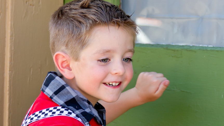 young boy wear in check short and red jumper with lollipop knocking at a green door