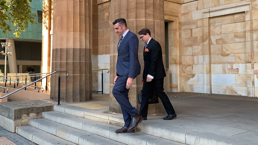 Two men in suits walk down stairs outside a sandstone building