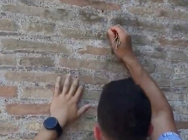 A close up of someone holding a key carving their name into bricks. 