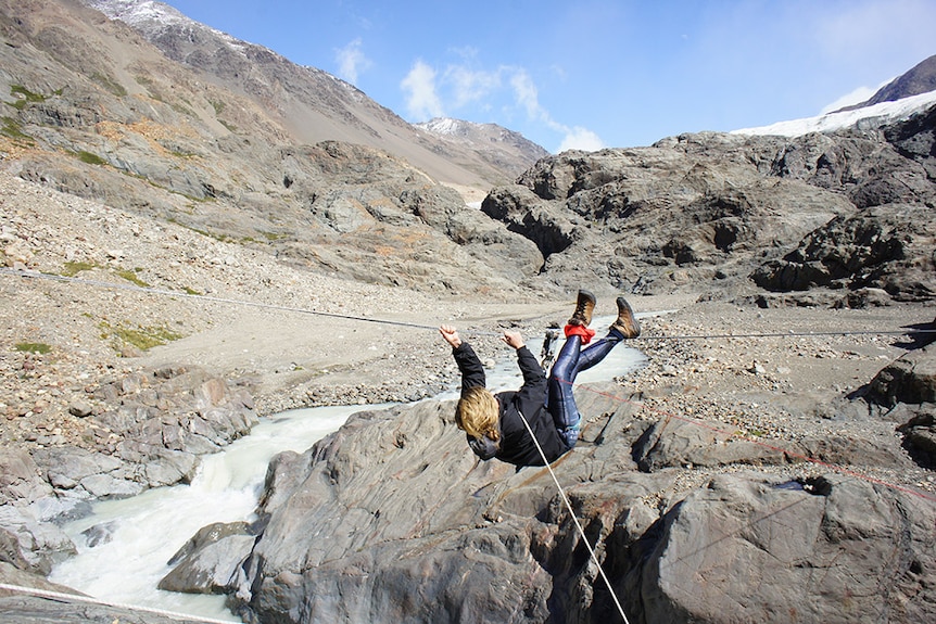 a woman hanging on a rope in front of cliffs