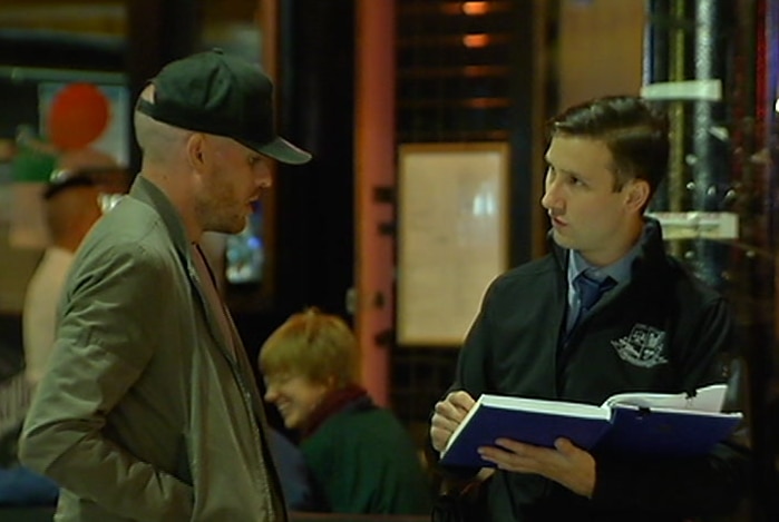 A police officer takes notes while speaking to a man in a baseball cap.