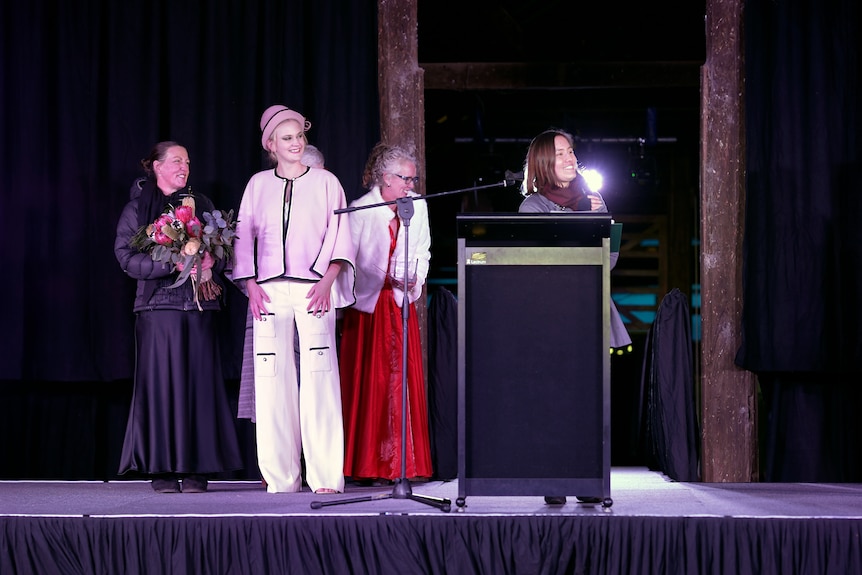 A young girl and women stand on a stage to accept an award.