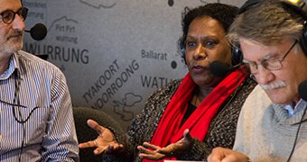 Two men listen as a woman talks. All wear radio headsets with microphones.