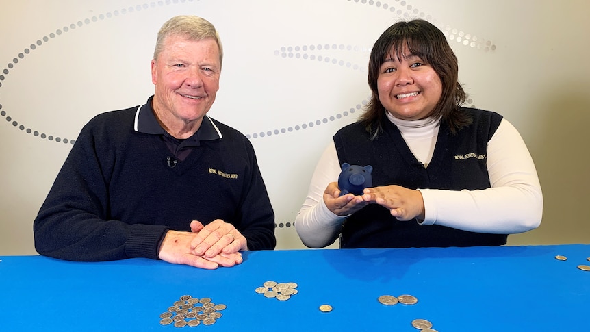 Man and woman pose for photo with coins on table, woman holds piggy bank