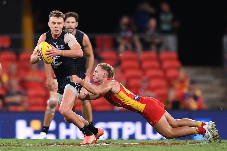 A Carlton AFL player holds the ball as he is tackled by a Gold Coast Suns opponent.