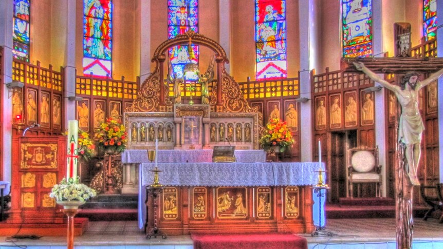 A colourful church altar with a large cross and painted glass windows.