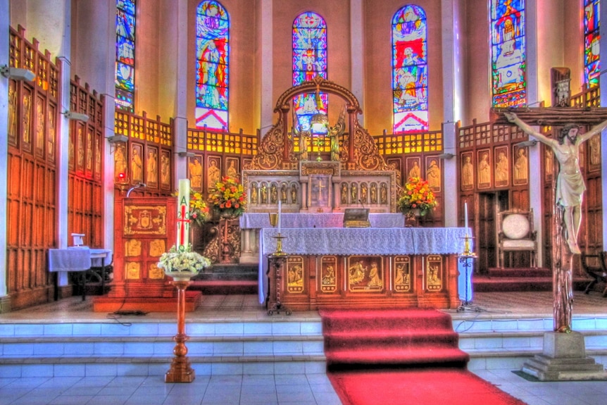 A colourful church altar with a large cross and painted glass windows.