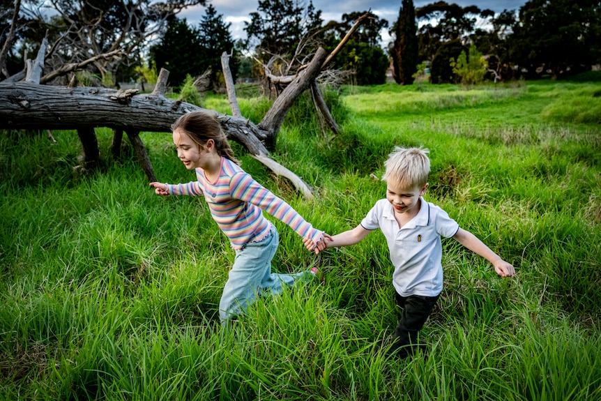 Two young white kids holding hands, running through long grass